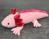 Weighted pink axolotl plush with red frills, full-body side view on a gray wood floor