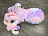 Purple pink blue weighted octopus plush on gray wood surface showing tie-dye head and coiled tentacles