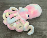 Side-back view of cotton-candy weighted octopus showing pastel fabric variation in pink, blue and yellow with curly plush stretch tentacles.