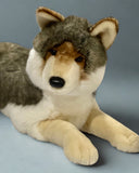 Close up view of Jumbo 37" weighted wolf plush in laying pose with head slightly cocked for realistic look. Thick plush gray and brown fur, creamy underbelly and muzzle, and thick chunky paws.
