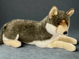 Realistic wolf plush in a lay-down pose, gray and tan coat with white chest, side view on a gray background