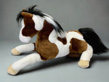 Weighted 27" brown and white paint horse plush lying on a gray surface, soft coat and realistic look.