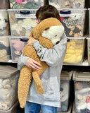 Adult holding a large weighted sea otter plush on shoulder to show hugging pose and size