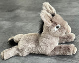 Side/top profile of weighted donkey plush showing long body, black mane and tail tuft; 18-inch laying pose.