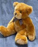 Classic weighted teddy bear with caramel plush fur and brown bow sitting on gray surface.