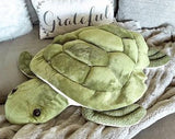 “36-inch weighted sea turtle plush in green, blanket-like shell resting on a sofa.”