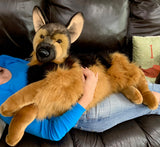 Person cuddling a 40" oversized German Shepherd weighted plush on a couch, showing realistic size and softness.