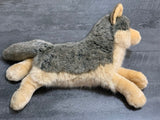Weighted wolf plush lying on its belly, grey fur with cream legs and muzzle on gray floor, 26 inches long.