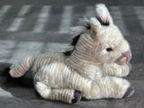 Side angle of weighted zebra plush with hind legs tucked forward highlighting soft hooves, ears, and mane; cuddly 19-inch stuffed animal.