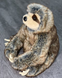 Three-quarter sitting view of weighted sloth plush showing long wraparound arms and fluffy coat; premium calming plush.