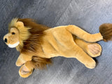 Top-down view of weighted lion plush slaying on it's side showing length and tail; tan coat with brown mane.