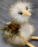 Weighted ostrich plush, 11 inches sitting, fluffy cream and tan feathers, long lashes and soft beak, sitting pose on gray surface.