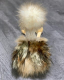 Back of weighted ostrich plush showing fluffy cream head and multi-tone tan feathered body with dangling legs on gray surface.