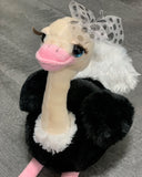 Close-up of weighted ostrich plush with polka-dot bow, black body, white tail, and pink beak.