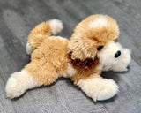 Weighted Goldendoodle plush in a floppy lay-down pose on gray wood surface