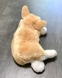 Back view of side-lying weighted corgi plush showing tan fur and white paws on gray surface.