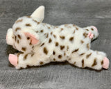Side view of weighted spotted pig plush lying flat; white fur with caramel spots and floppy legs.