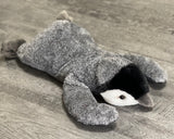 Belly-down weighted penguin plush, gray chick with black head and flippers outstretched on a wood floor.