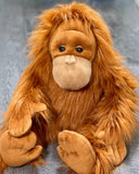Large weighted orangutan plush with shaggy rust-orange fur, sitting pose on wood floor, front view