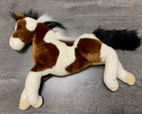 Top-down side view of weighted paint horse plush with floppy legs and realistic markings laying on a gray surface.
