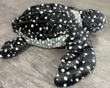 Side view of black and white spotted weighted sea turtle plush showing its ridged shell, realistic head and eyes, and large front flipper.