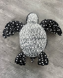 Underside of weighted black and white spotted sea turtle plush showing gray belly with white markings and black spotted flippers.