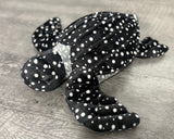 Three-quarter view of black and white spotted weighted sea turtle plush showing raised shell ridges and extended flippers.