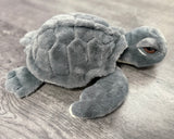 Gray weighted sea turtle plush with oversized floppy head, sleepy brown eyes, and soft textured shell, side view.