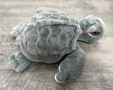 Close-up of adorable gray weighted sea turtle showing its rounded plush shell, sleepy eyes, and soft front flippers.