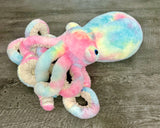 Tie-Dye Pink, blue and yellow weighted octopus plush on wood surface with textured tentacles arranged in front.