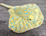 Blue spotted weighted stingray plush with golden-yellow fur, bright blue spots, wide weighted wings, and yellow-rimmed eyes.