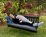 Person lying on a black wood swing with a 32-inch weighted gray seal plush down their body, 18lb in a garden setting.