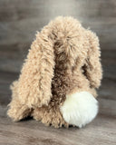 Side back view of weighted curly bunny plush with fluffy white tail and long floppy ears.