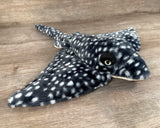 Side angle view of black with white spots weighted stingray plush showing realistic eyes and wide 24" wing span.
