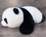 Soft black and white weighted panda stuffed animal lying on its belly.  Side-angle view.