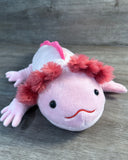 Pink weighted axolotl plush with a smiling face, fluffy coral-pink gills, black eyes, and four little feet.