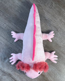 Overhead view of pink weighted axolotl plush with four spread-out legs, fluffy pink gills, and bright pink ridge along its back and tail.