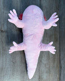 Underside of 19-inch pink weighted axolotl plush showing its smooth pink belly, four soft legs, and long tapered tail.