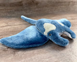 Side-front view of a blue weighted manta ray plush with soft, wide wings, curved head fins, a sweet smile, and gray markings, 6lbs.
