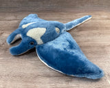 Angled view of ultra-soft blue weighted manta ray plush showing its 24" broad wingspan, long tail, and distinctive head fins.