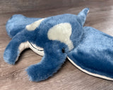 Close-up of blue weighted manta ray plush showing its soft blue fur, curved head fins, black eyes and a sweet smile.