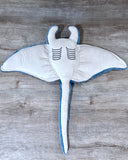Underside of blue weighted manta ray plush showing its smooth light gray belly, embroidered gill markings, and long tail.