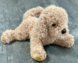 Weighted tan doodle plush in a relaxed lay-down pose on gray wood background