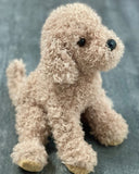 15-inch weighted doodle dog plush with curly tan coat, sitting on gray wood background