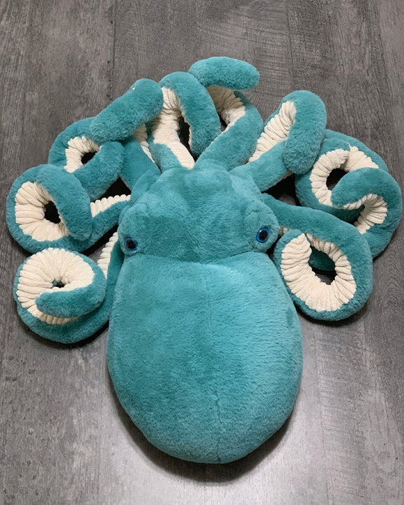 Giant teal weighted octopus plush with cream-lined curled tentacles, top-down view on wood floor