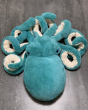 Giant teal weighted octopus plush with cream-lined curled tentacles, top-down view on wood floor